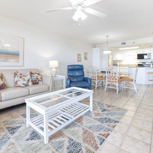 Living area features a light-colored sofa with decorative pillows, a glass coffee table, and a dining area with seating