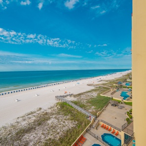 A panoramic view showcases the pristine white sand beach lined with umbrellas and a glimpse of the inviting pool area below