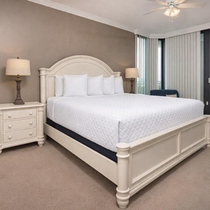 Master bedroom featuring a plush king bed, stylish lamp, and large balcony windows for scenic views