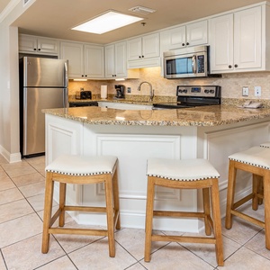 Bright, fully-equipped kitchen features a granite countertop, white cabinetry, and four stylish bar stools for casual dining