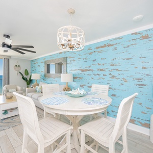 Brightly decorated living space features a round dining table, comfortable seating, and expansive views of the beach