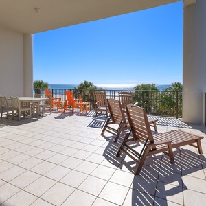 This spacious wrap-around balcony features wooden lounge chairs and a dining table, offering a stunning beachfront view
