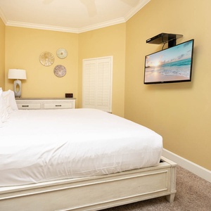 Cozy guest bedroom featuring a king bed, mounted TV, and cheerful yellow walls for a relaxing retreat