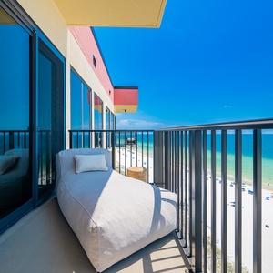 Relax on the cozy lounge chair of this balcony, offering breathtaking views of the serene beach and vibrant blue waters