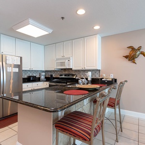 The kitchen features stainless appliances, granite countertops, and colorful bar stools, perfect for casual dining