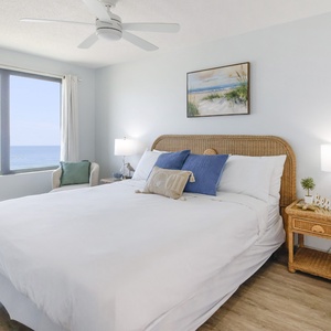 This bedroom features a cozy bed with blue accents and a stunning beachfront view through large windows