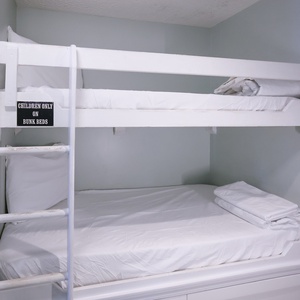 This cozy bunk area features white bedding and a playful sign, perfect for kids' adventures during their stay