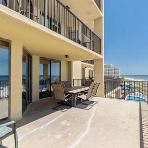 The spacious extended balcony features a dining table with chairs, offering a beautiful view of the beach and pool area
