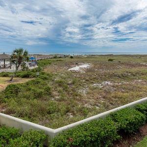 Lush greenery and palm trees frame the view of the beach, with a glimpse of the pool area and boardwalk in the distance