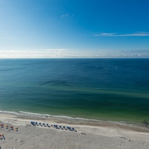 The beachfront balcony view features vibrant umbrellas on the sandy shore, inviting relaxation and fun