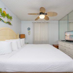 The master bedroom features a cozy bed with white linens, tropical decor, and warm lighting for a relaxing retreat
