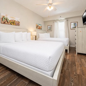 Two comfortable queen beds with white linens and a ceiling fan create a relaxing atmosphere in this cozy guest room
