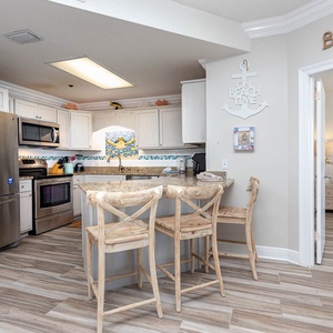 Kitchen features a granite breakfast bar with stools, modern appliances, and coastal decor enhancing the inviting atmosphere