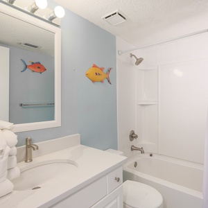 The bathroom features a clean white vanity, colorful fish decor, and a relaxing tub-shower combo for a refreshing stay