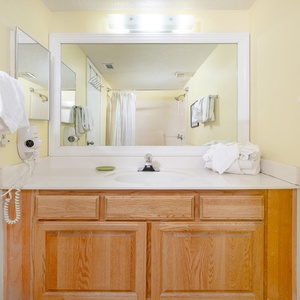 Bright guest bathroom featuring a spacious vanity with a sink, ample towels, and a shower area behind a curtain