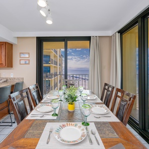 The dining area features a wooden table set for six, with a view of the beach visible through large sliding glass doors