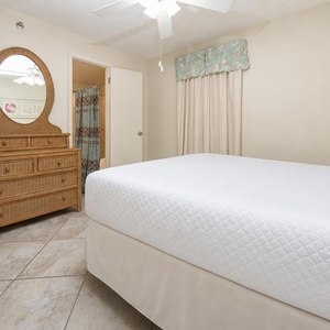 Cozy guest bedroom features a queen bed, a wicker dresser with a mirror, and soft beige walls, creating a serene atmosphere