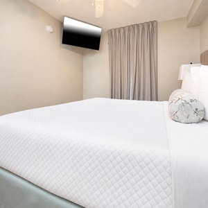 Rest in the comfortable bedroom featuring a king bed, a mounted TV, and soft curtains for a peaceful retreat