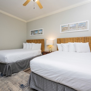 This guest bedroom features two queen beds with woven headboards, soft linens, and beach-themed artwork for a relaxing stay