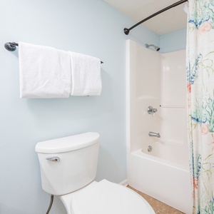 The guest bathroom featuring a tub/shower combo with a colorful coastal shower curtain and fresh white towels