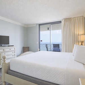 The master features a king bed, a TV, and access to a balcony with a serene view of the beach