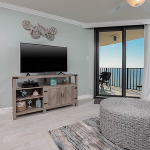 Living area features a TV, wooden console, a cozy gray armchair, and sliding glass doors leading to the balcony with a view