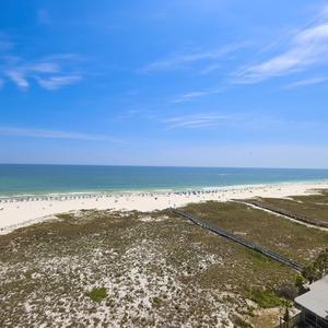 Expansive view of the beach with white sand, inviting turquoise waters, and beachgoers enjoying the sunny day