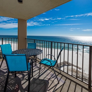 Relax on the balcony with turquoise chairs, a round table, and breathtaking views of the sandy shore and sparkling water