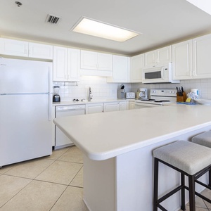 White cabinetry complements the spacious counter, featuring a breakfast bar, white appliances, and seating for four