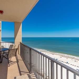 A cozy balcony features a round table and chairs, offering a serene view of the beach and tranquil blue waters