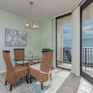 Dining area features a glass table with wicker chairs, offering a view of the beach through expansive sliding glass doors