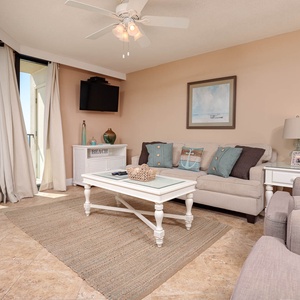 The inviting living room features a light-colored sofa with queen sleeper, a stylish coffee table, and a view of the beach