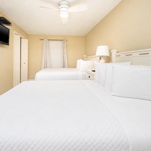 Guest bedroom featuring two comfortable queen beds, a wall-mounted TV, and soft natural light from the window