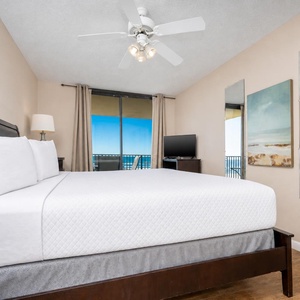 Master bedroom featuring a king bed, a TV, and large windows with a view of the beach, complemented by soft, neutral decor