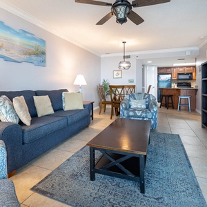Cozy living area features a blue sofa with decorative pillows, a coffee table, and a dining space leading to the kitchen
