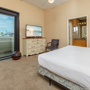 Cozy master bedroom featuring a king bed, a TV, and a sliding door leading to a balcony with views of the surrounding area
