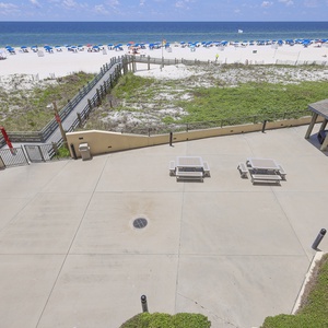 Pool and patio area with picnic tables leading to a beach adorned with colorful umbrellas