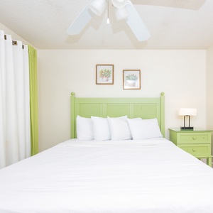 The guest bedroom features a light green headboard, queen bed, soft white linens, and vibrant curtains