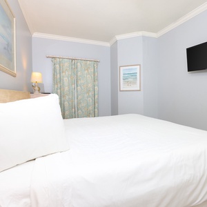 This cozy bedroom features a comfortable bed, soft blue walls, and a wall-mounted TV for relaxing evenings