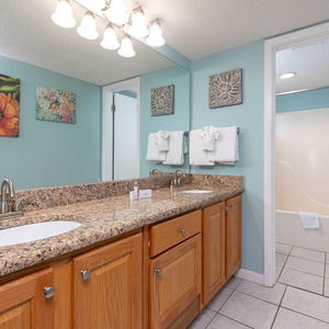 Bright master bathroom featuring a granite countertop, dual sinks, and colorful floral artwork against a soothing blue wall