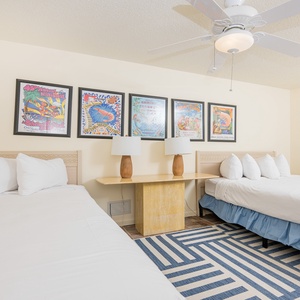 Cozy guest room featuring two queen beds, vibrant artwork, and a stylish rug for a welcoming coastal vibe