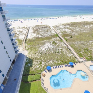 Stunning view of the beach, a pool area featuring umbrellas, and a winding path leading to the shoreline