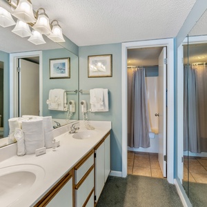 Bright master bathroom featuring a double sink vanity, large mirrors, and a tub/shower combo, accented by soft blue walls