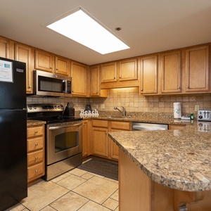 This fully-equipped kitchen features warm wood cabinetry, granite countertops, and a convenient breakfast bar