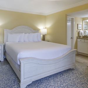 Master bedroom featuring a king bed with white linens, nightstands, and an adjoining bathroom area