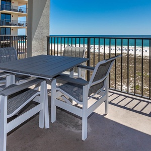 Outdoor balcony features a dining table with four chairs, offering a view of the beach and turquoise gulf waters