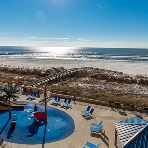 The view showcases a vibrant pool area with the pirate ship splash park, leading to a serene beach and sparkling water