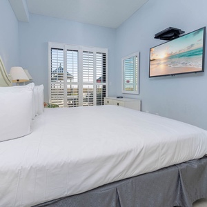 Brightly decorated master bedroom featuring a plush king bed, a wall-mounted TV, and patio to a charming outdoor view