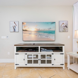 A cozy living area features a large TV above a stylish cabinet, complemented by beach-themed artwork and soft natural light