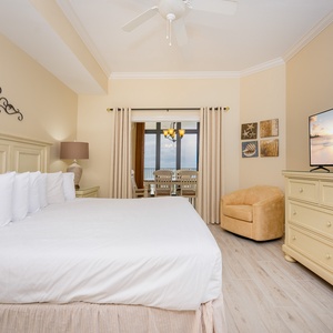 Relaxing master bedroom featuring a plush king bed, a flat-screen TV, and a cozy seating area with a view of the balcony